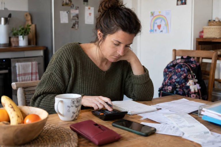 Une femme est assise à une table, une calculatrice à la main, entourée de papiers