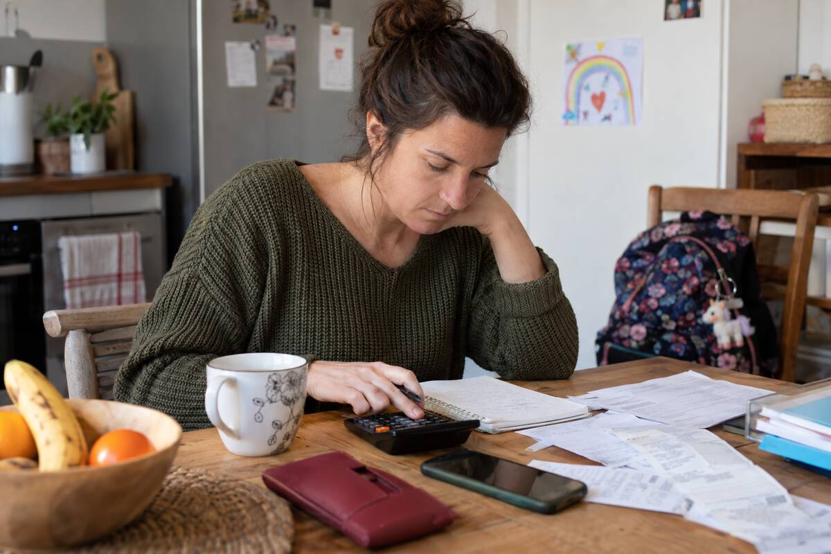 Une femme est assise à une table, une calculatrice à la main, entourée de papiers